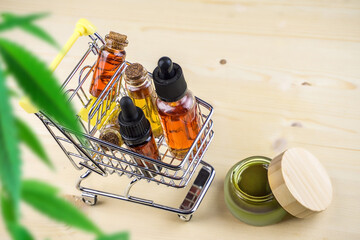 Cannabis CBD oil shopping concept, Medical marijuana oils in miniature shopping cart on wooden backdrop