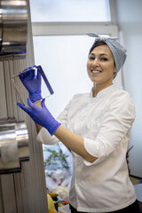 Cheerful woman chef in white uniform looking on metal bakeware meal mold dishes for baking