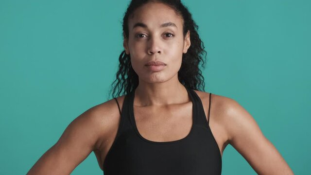 Young beautiful African American woman dressed in sport bra looking confident after workout over blue background. Sporty girl