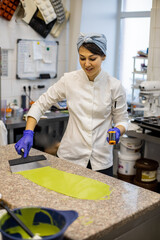 Woman confectioner in uniform pouring liquid matcha tea chocolate on table from bowl at cuisine