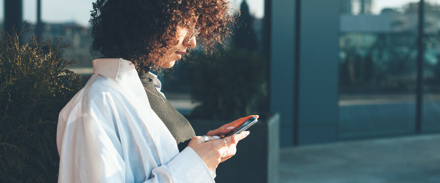 Side view photo of a curly haired woman chatting on mobile with friends