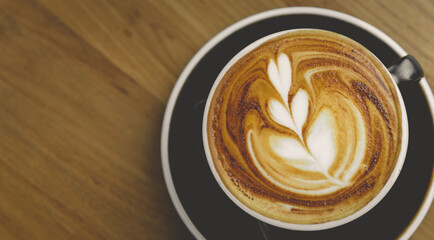 Top view of fresh brewed coffee with beautiful latte art on wooden table in cafe with copy space. Coffee break recreation relaxation
