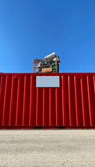 Knallroter Container, darauf ein Metallbehälter gefüllt mit alufarbenen  Behälter und grünen Plastik, blauer Himmel