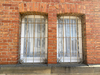 Fototapeta na wymiar Zwei Fenster, helle Vorhänge, verrostete Gitter, Backsteinwand, Fenstersims, Sandsteinwand