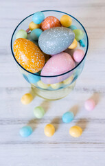 Easter sweets and pastel colored eggs in a beautiful glass vase. Easter celebration concept. Top view.