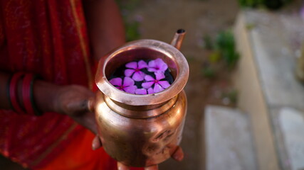 Closeup shot of Copper kalash filled with sacred water to offer God. Human hand holding Kalash to religious morning prayer.