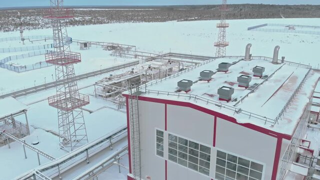 In winter, the flight of the quadcopter. View from above. Close-up shot of an oil and gas field. Shown is a white building with red stripes, towers and other industrial objects.