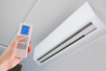 Man's hand using remote control open The air conditioner is cooled to 25 degrees Celsius in his bedroom. Health concepts and energy savings