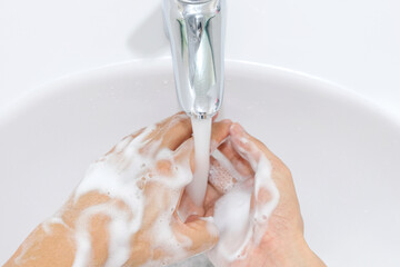 Hands of woman wash their hands in a sink with foam to wash the skin and water flows through the hands. Concept of health, cleaning and preventing germs and coronavirus from contacting hands