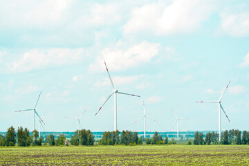 many windmills stand on a large field spinning in the day against a sunset orange sky. Alternative...