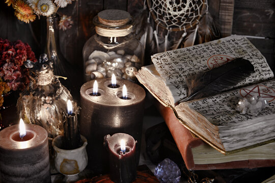 Burning candles and open book with magic spells on witch table.