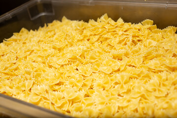 A view of a large container of prepared cooked bowtie pasta, in a restaurant kitchen setting.