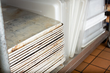 A view of a stack of metal baking sheets, in a restaurant kitchen setting.