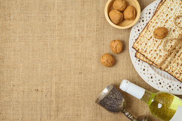 Jewish holiday Passover concept with matzah, wine bottle and walnuts on sackcloth background