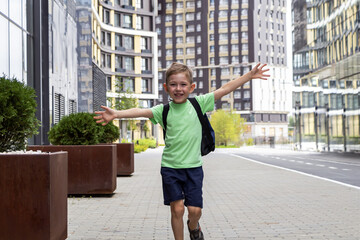 Happy smiling schoolboy with backpack running and waving hands outdoors. Children's happiness