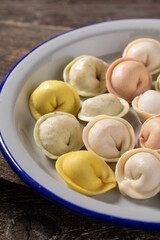 Traditional Russian dumplings made from multi-colored dough. Dumplings on a wooden board in an enamel plate. Cooking concept.