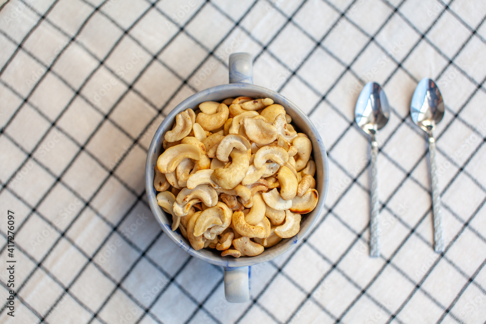 Poster a plate of cashew nuts on a nice napkin and two spoons next to it.