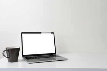 Fototapeta premium Modern contemporary workspace with blank screen laptop computer and coffee cup on office desk table on white background for copy space. Home office workplace concept.