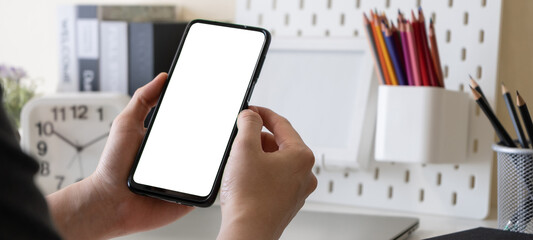 Male freelancer or business man using mobile phone with blank white screen for mock up at home office table. Work at home concept.