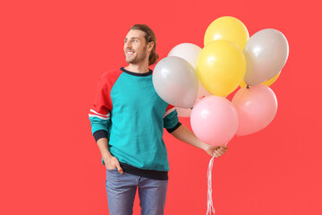 Handsome young man with balloons on color background