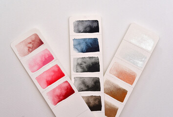 Color palette, three strips of paper with pink, metallic and gray shades, watercolor paper.