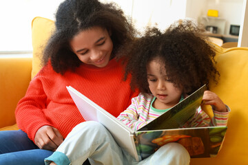 Cute African-American sisters reading book at home