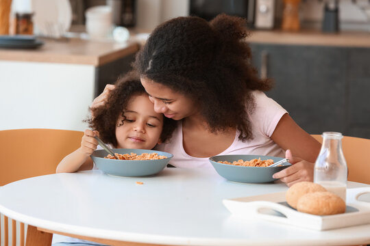Cute African-American sisters having breakfast at home