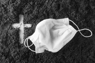 A cross inscribed on the ground and a medical mask. The concept of memory of dead people during the...