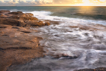Amazing beach sunset with endless horizon and incredible foam waves. Stone hills foreground