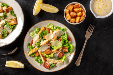 Caesar salad with grilled chicken, romaine and Parmesan, shot from the top on a black background with copy space