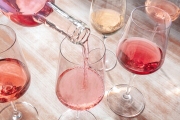 Pouring rose wine, glasses of various wine on a wooden table