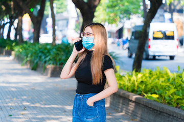 A blonde hair asian girl is using smartphone with a face mask at public during Covid-19