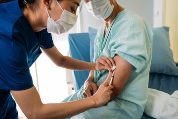 Closeup of young female doctor in uniform wearing face mask while giving vaccination injection to young male patient wearing a mask for safety against covid-19 pandemic