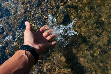 Hands touch the natural water in the forest, the water is clear until you can see small rocks in the water.