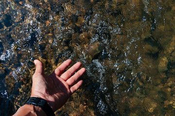 Hands touch the natural water in the forest, the water is clear until you can see small rocks in the water.