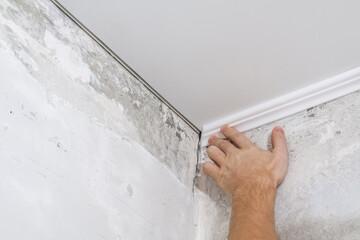 Worker fixes the plastic molding to the ceiling. Installation of ceiling cornice.
