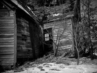 Fototapeta na wymiar A black-and-white rural Missouri winter landscape detail of a delapidated abandoned house partially covered in snow looking through an open door to a window on the opposite wall.