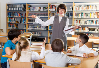 Portrait of young female librarian and diligent schoolkids during classes in school library..