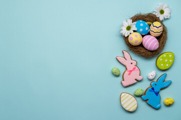 Fototapeta na wymiar Easter banner. Spring holiday ornament. Festive bakery food decoration. Colorful icing gingerbread bunny cookie painted eggs set flowers in nest isolated on blue copy space background.