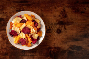 Vegetable chips, shot from above on a dark rustic wooden background with copy space
