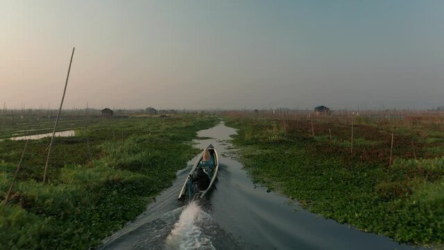 Traditional long tail boat travels in small waterway of Floating Gardens at Inle