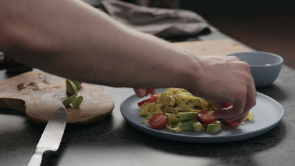 man add cherry tomatoes to pesto fettuccine on blue plate