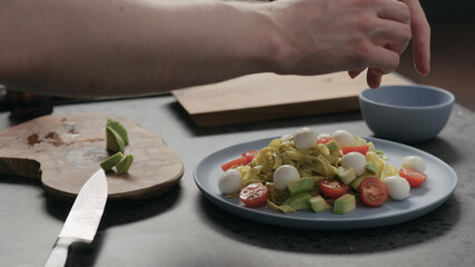 man add mozzarella to pesto fettuccine on blue plate