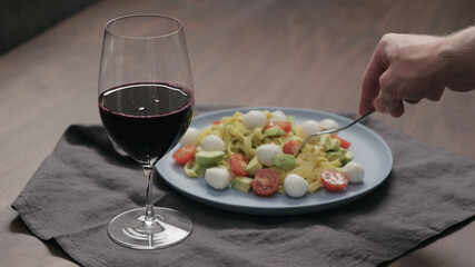 man eatings fettuccine with pesto, tomatoes and mozzarella with glass of red wine