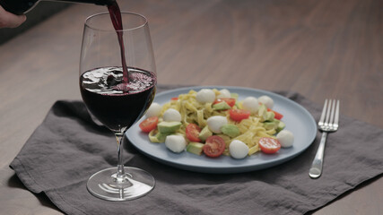 pour red wine into wineglass with bowl of fettuccine on background