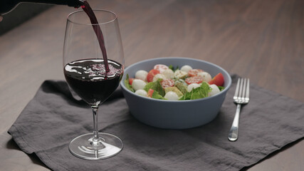 pour red wine into wineglass with bowl of salad on background