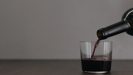 pour red wine into tumbler glass on wood table with copy space