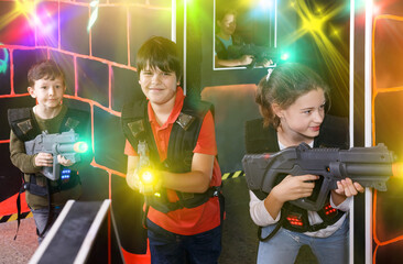 Fototapeta na wymiar Glad girl aiming laser gun at other players during lasertag game in dark room