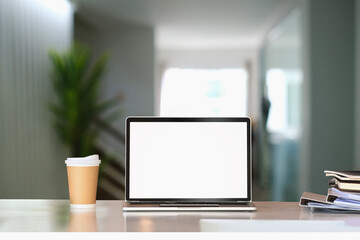Front view of computer laptop with blank screen, coffee cup and document on white table in living room.