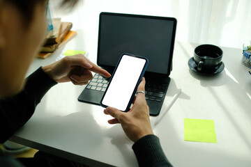 Close up view of young man holding mobile phone with blank screen while sitting in front of computer tablet at home office.